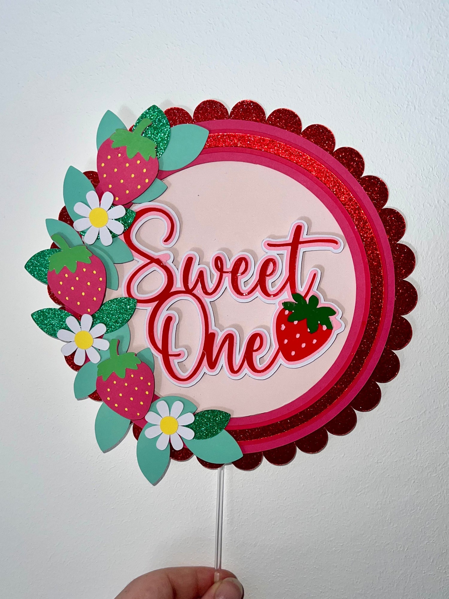 Decorative cake topper with 'Sweet One' text and strawberry design on a white background